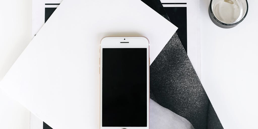 An eye-catching flat lay of a smartphone displaying a lead generation app, surrounded by marketing materials like brochures, business cards, and a laptop. The background is a wooden table with a plant and a cup of coffee, conveying a modern and tech-savvy approach to acquiring leads.