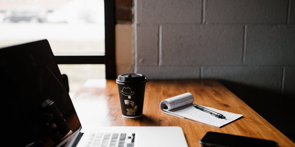 An overhead shot of a workspace featuring a notebook with handwritten notes about Instantly.ai, a smartphone displaying the app, and a cup of coffee, creating a cozy and productive atmosphere.