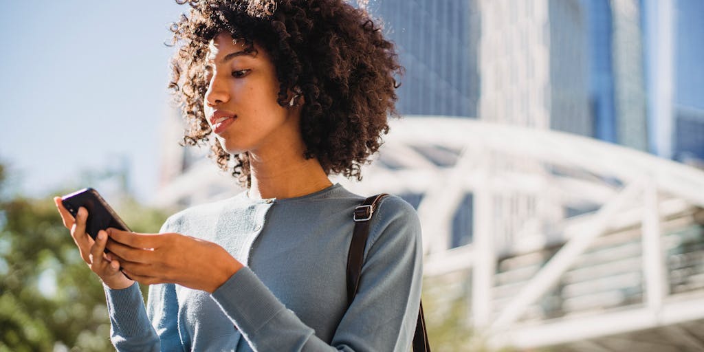 A close-up shot of a person holding a smartphone displaying the Rocketreach app, with a blurred background of a city skyline. This image represents the accessibility and convenience of using Rocketreach's pricing options on-the-go.