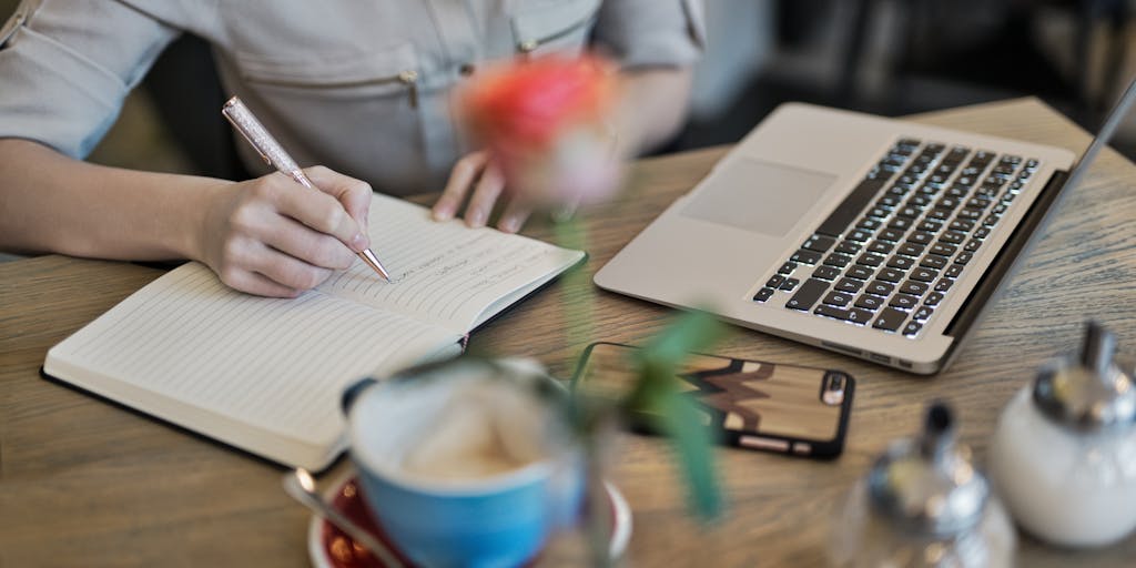 An overhead view of a desk with a laptop open to the Sales Loft pricing page, alongside a cup of coffee and a notepad filled with handwritten notes. The scene captures a moment of contemplation and decision-making about pricing strategies.
