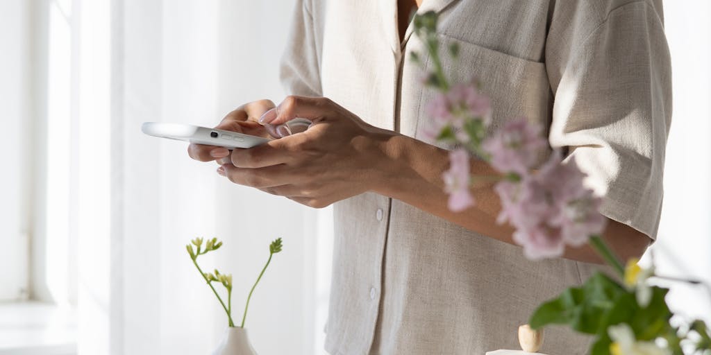 A close-up shot of a hand holding a smartphone displaying the Findymail pricing page, with a blurred background of a coffee shop setting. The focus is on the screen, highlighting the pricing options, while the warm ambiance of the café adds a casual and relatable feel.