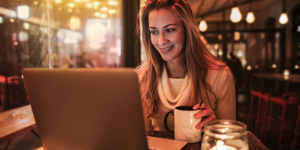 A conceptual photo of a person holding a magnifying glass over a Waalaxy pricing page on a laptop. The focus should be on the magnifying glass, highlighting the details of the pricing. The setting should be a cozy coffee shop, suggesting a casual yet serious approach to evaluating business expenses.