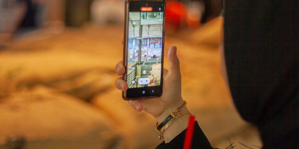 A close-up shot of a hand holding a smartphone displaying the Uptics Pricing page, with a blurred background of a bustling coffee shop. The focus is on the screen, showcasing the pricing tiers, while the ambient environment suggests a modern, tech-savvy lifestyle.