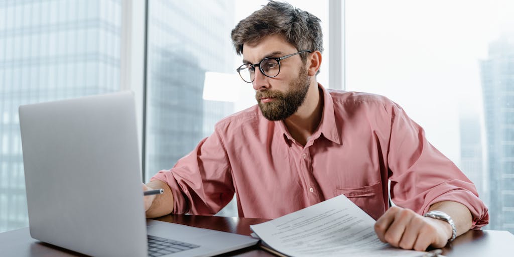 An overhead view of a desk cluttered with various pricing strategy documents, sticky notes, and a laptop open to the Alfred Pricing website. A cup of coffee sits beside the laptop, creating a warm and inviting atmosphere for brainstorming pricing strategies.