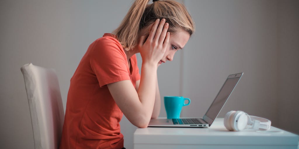 A person sitting at a desk, looking thoughtfully at a laptop screen displaying Anymail Finder's pricing page. The scene captures a moment of decision-making, with a cup of coffee and a pen in hand, symbolizing the importance of choosing the right pricing plan.