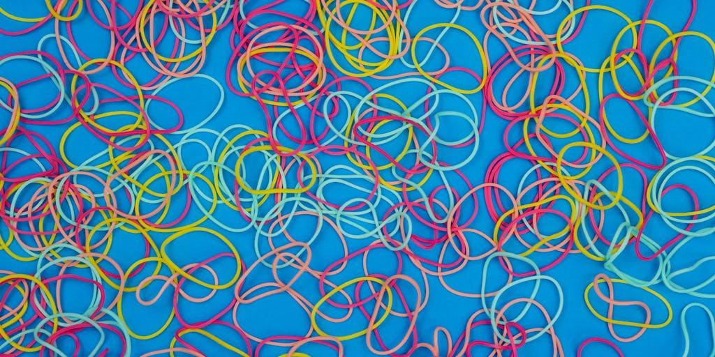 A close-up shot of a hand holding a flexible rubber band, symbolizing the elasticity of pricing. The background features a blurred computer screen displaying the Elastic Email pricing page, emphasizing the connection between flexibility and cost.