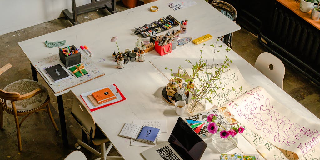 An overhead view of a workspace with various clay tools and materials scattered around, alongside a laptop displaying the Clay.com pricing page. The scene conveys a creative and productive atmosphere, showcasing the intersection of art and business.