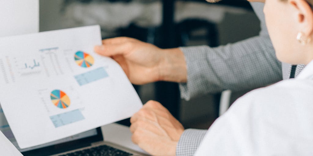 A close-up shot of a sales team gathered around a table, analyzing a colorful pricing strategy chart on a laptop screen. The atmosphere is collaborative, with sticky notes and coffee cups scattered around, symbolizing brainstorming and teamwork in sales enablement.