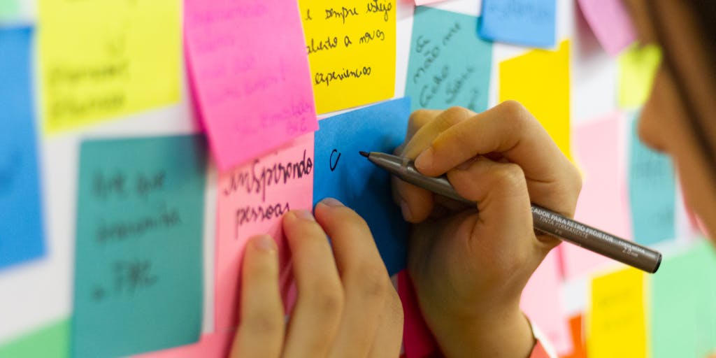 An overhead view of a desk cluttered with sticky notes, each containing different creative LinkedIn InMail subject lines. A hand is seen writing on a notepad, emphasizing the brainstorming process for effective communication.