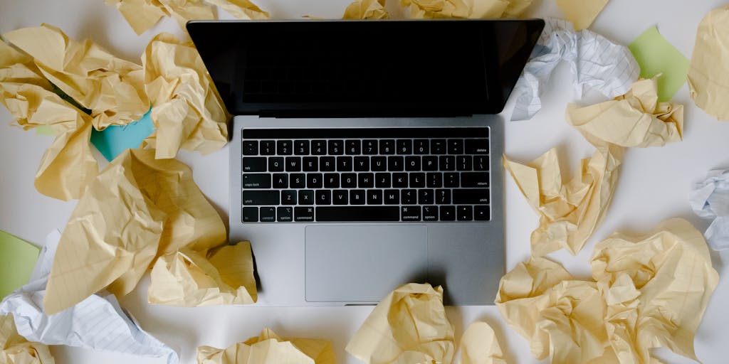 An overhead shot of a desk cluttered with sticky notes, each labeled with different LinkedIn account details (like usernames, passwords, and profile tips). A laptop is open in the center, displaying a LinkedIn dashboard, symbolizing the organization needed to manage multiple accounts.