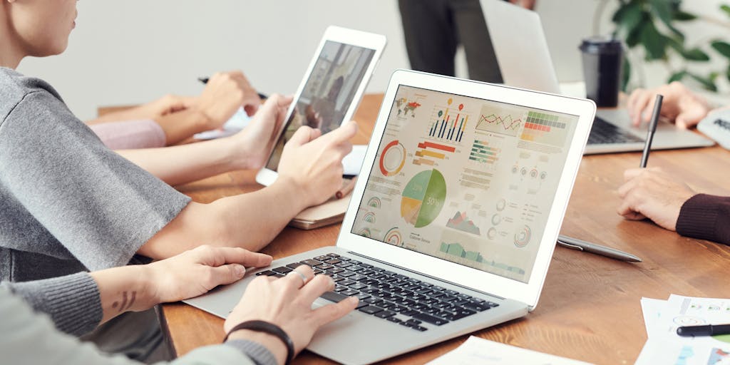 A split-screen image showing two professionals at their desks, one using LinkedIn Recruiter and the other using Sales Navigator. The recruiter is surrounded by resumes and candidate profiles, while the salesperson has charts and sales metrics on their screen. The contrasting environments highlight the different focuses of each tool.