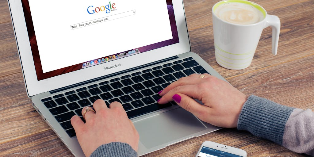 A close-up shot of a laptop screen displaying a Google search page with the query 'LinkedIn profiles' typed in. The background features a blurred office environment, symbolizing a professional setting. The laptop is surrounded by notes and a coffee cup, suggesting a busy workday.